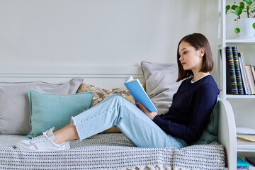 Young woman reading book, relaxed sitting on couch at home