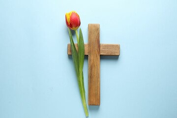 Easter - celebration of Jesus resurrection. Wooden cross and tulip on light blue background, top view