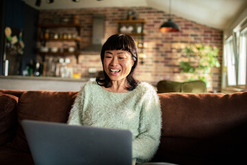 Smiling woman gesturing at laptop on the couch at home