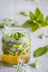 Pickled wild garlic blossoms on white wooden background, vertical