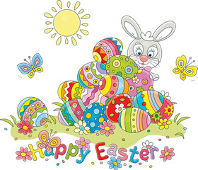 Obraz na płótnie Canvas Greeting card with a happy Easter bunny and a pile of colorfully painted gift eggs on a pretty sunny lawn with spring flowers and merry butterflies fluttering around, vector cartoon illustration