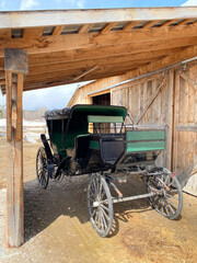 Fototapeta na wymiar Old carriage in the village. Antique carriole in a stable. Vintage black and green western cart with large wooden wheels. Old horse-drawn carriage in a barn.