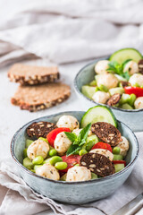 Summer salad with cucumber, mini tomatos, mini mozzarella and soybeans on white wooden background