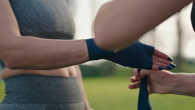 Closeup of a female fitness trainer's hands expertly wrapping a student's hands with blue boxing wraps, prepping for a training session.