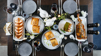 Easter holidays table with baked meat tenderloin, rib eye meat, ribs, lamb thigh, wine glasses,...