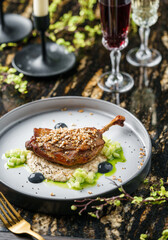 Baked duck leg with vegetable puree and sauce on plate over marble background with wine glass. Holiday healthy food, top view