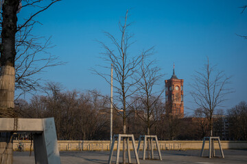 Rot rathaus or red town hall sticking out from alexanderplatz park and tree tops in early spring...