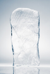 Crystal clear natural ice block in light blue tones on a white reflective surface.