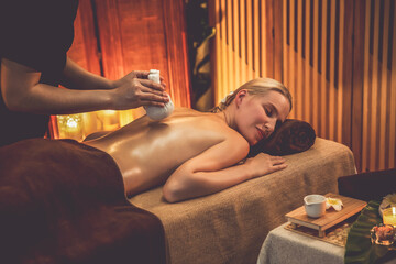 Hot herbal ball spa massage body treatment, masseur gently compresses herb bag on woman body....