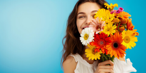 Studio photograph of a young smiling woman holding a bouquet of multicolored gerbera daisies against a blue background