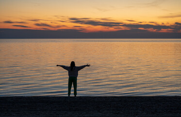 A teenage girl is meditating and exercising on the seashore watching a beautiful sunset. Sithonia, Greece, Halkidiki. Paradisos Beach in Neos Marmaras.
