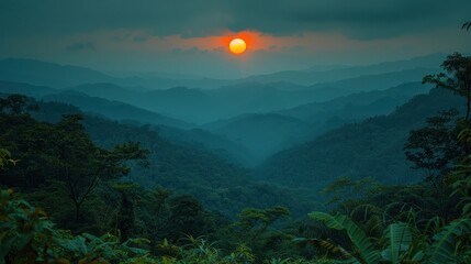 Fototapeta na wymiar the sun is setting over the mountains in the foggy area of a tropical valley with trees and bushes in the foreground.