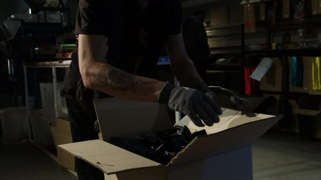 Strong man worker skillfully places coffee packages into cardboard box. Young man in latex gloves closes box with easy movements