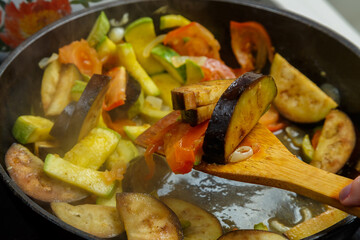 Vegetables fried in spices in a frying pan with a wooden spatula.