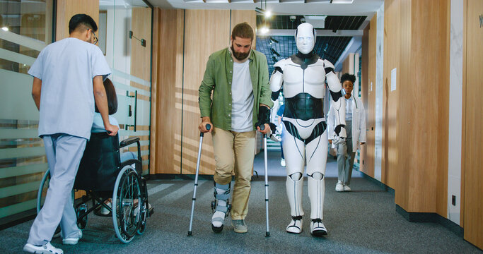 Young beautiful injured patient struggling to walk with crutches and helpful robot assistant in future hospital helping. Artificially intelligent white bot working at clinic assisting people.