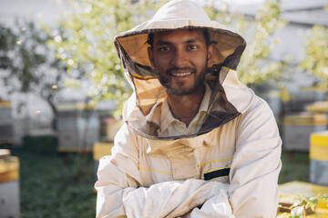 Portrait of a happy Indian male beekeeper working in an apiary near beehives with bees. Collect...