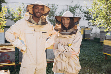 Two beekeepers in protective uniform standing together near the wooden beehives on a small...