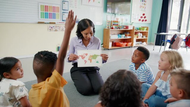 Female primary or elementary school teacher showing map to students sitting on floor in multi-cultural classroom in geography lesson - shot in slow motion