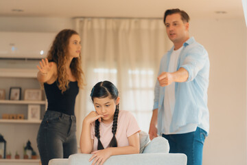 Annoyed and unhappy young girl sitting on sofa trapped in middle of tension by her parent argument in living room. Unhealthy domestic lifestyle and traumatic childhood develop to depression.Synchronos