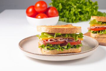 Close-up of two sandwiches with bacon, salami, prosciutto and fresh vegetables on rustic wooden cutting board. Club sandwich concept - 750911048