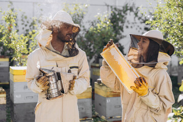 Couple of happy smiling beekeepers working with beekeeping tools near beehive at bee farm