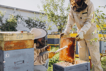 Couple of happy smiling beekeepers working with beekeeping tools near beehive at bee farm