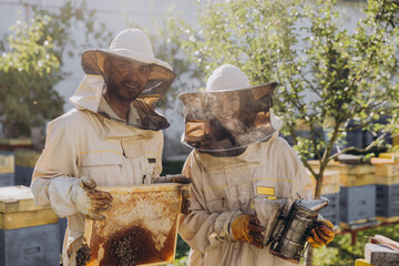 Couple of happy smiling beekeepers working with beekeeping tools near beehive at bee farm