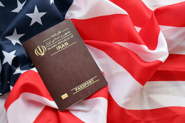 Red Islamic Republic of Iran passport on United States national flag background close up. Tourism...