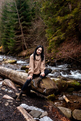 Young brunette woman explores new, magical, and fantastic places around the world. Portrait of cute young female relaxing and smiling in forest with stream. - 750919800