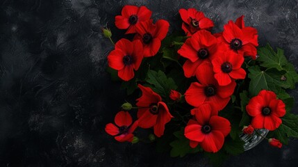 a group of red flowers sitting on top of a black table next to a green leafy plant on top of a black surface.