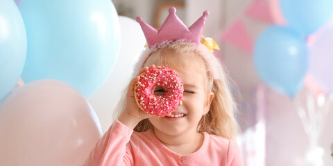 Cute little girl in crown with doughnut celebrating Birthday at home, closeup