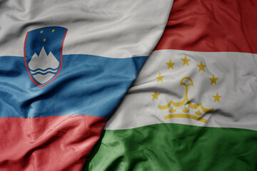 big waving national colorful flag of tajikistan and national flag of slovenia.