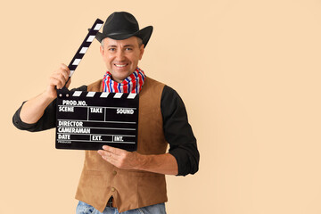 Mature actor dressed as cowboy with clapperboard on beige background