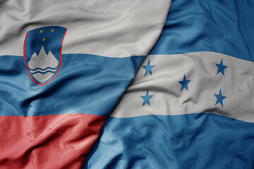 big waving national colorful flag of honduras and national flag of slovenia.