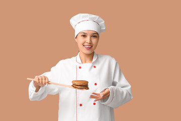 Young Asian female chef holding spatula with tasty pancakes on brown background