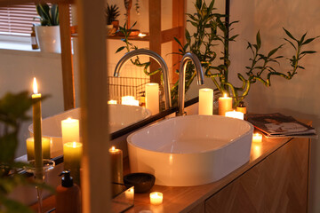 Sink with burning candles and bamboo stems in bathroom at night