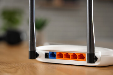 Modern wi-fi router on wooden table in room, back view