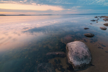 Tranquil sunset scene in winter time at lake coast with large rock in the foreground - 750934244
