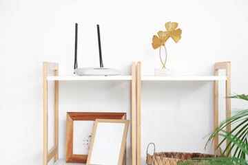 Modern wi-fi router on shelf near light wall