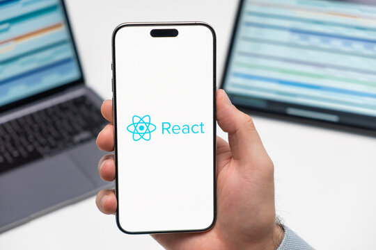 PRAGUE, CZECH REPUBLIC - JANUARY 21 2024: React logo on the screen of smartphone in mans hand on the workplace background. 