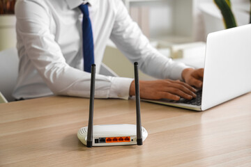 Modern wi-fi router on table of businessman using laptop in office, closeup