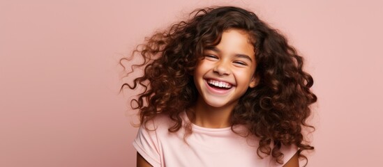A young girl with curly light brown hair is smiling widely while wearing a white t-shirt. The...