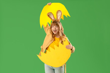 Young girl with Easter bunny ears and broken paper egg on green background