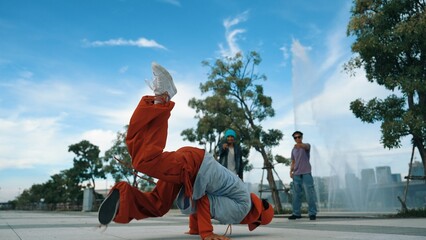 Asian skilled hipster doing freeze pose at camera surrounded by break dancer team near fountain...