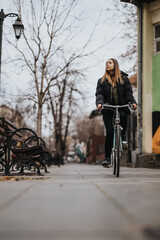 A woman enjoys a leisurely bike ride down a serene city sidewalk lined with bare trees and benches, embodying urban cycling and active lifestyle.