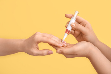 Female hands applying cuticle oil with pen on yellow background, closeup