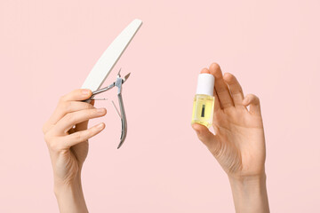 Female hands with bottle of cuticle oil, nail file and cutter on pink background