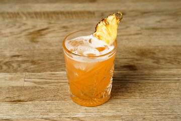 A cocktail with pineapple and ice on a wooden table