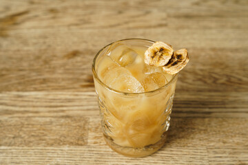 A cocktail with a slice of dried banana and ice on a wooden table