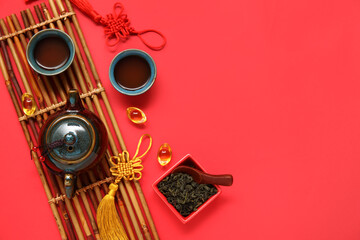 Bamboo mat with teapot, cups of tea and bowl with dry leaves on red background